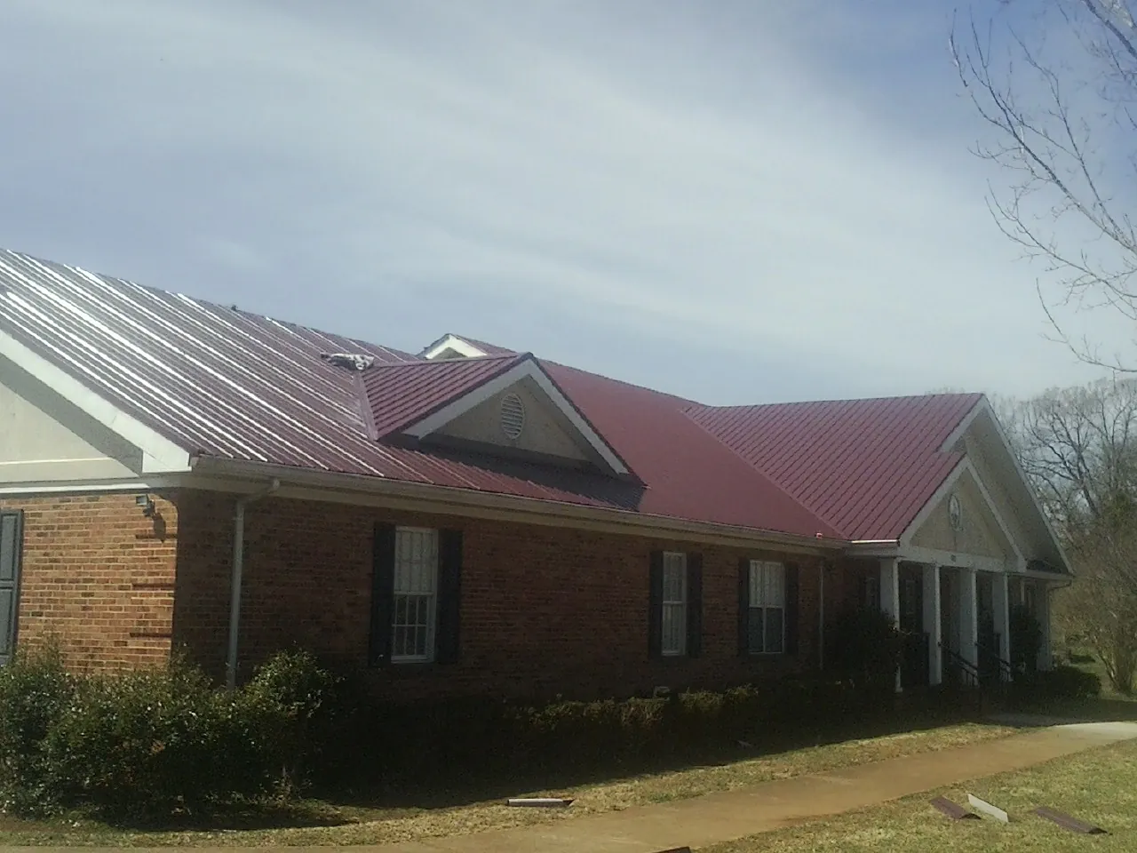 Red metal roof with gabled entries on a long brick building, from a Hail Damage Roof Repair job in Waldport