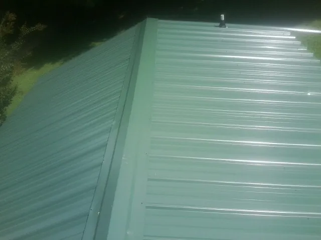 New green metal panels meeting at the ridge of a roof — Flat Roof Repair work by our crew in Waldport