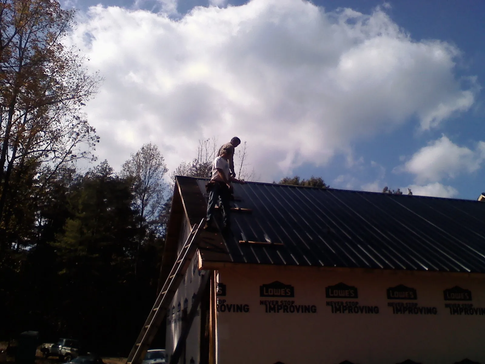 Roofer fastening dark metal panels high against a cloudy sky, from a Roof Inspection job in Waldport