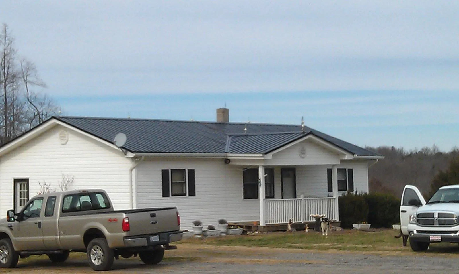 Finished dark metal roof on a white ranch home with work trucks parked in Waldport