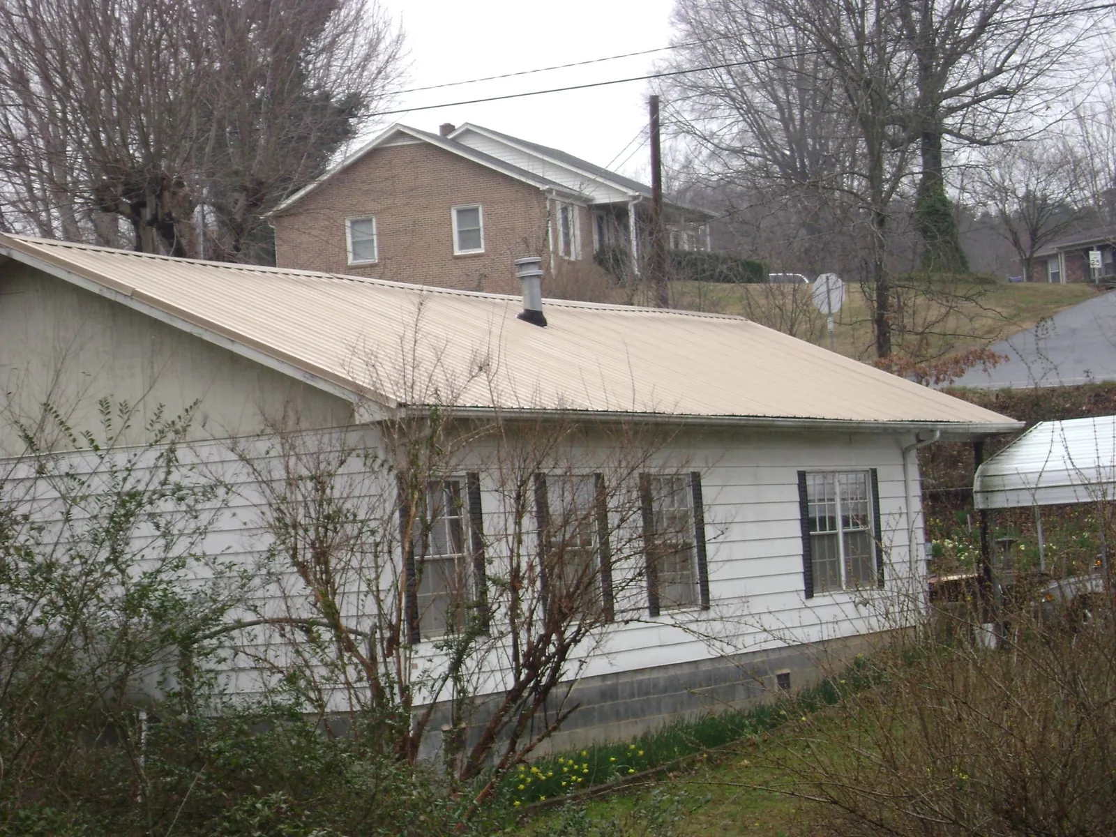 Tan metal roof on a white sided house set into a hillside — Commercial Roofing by Roofing Brothers in Waldport